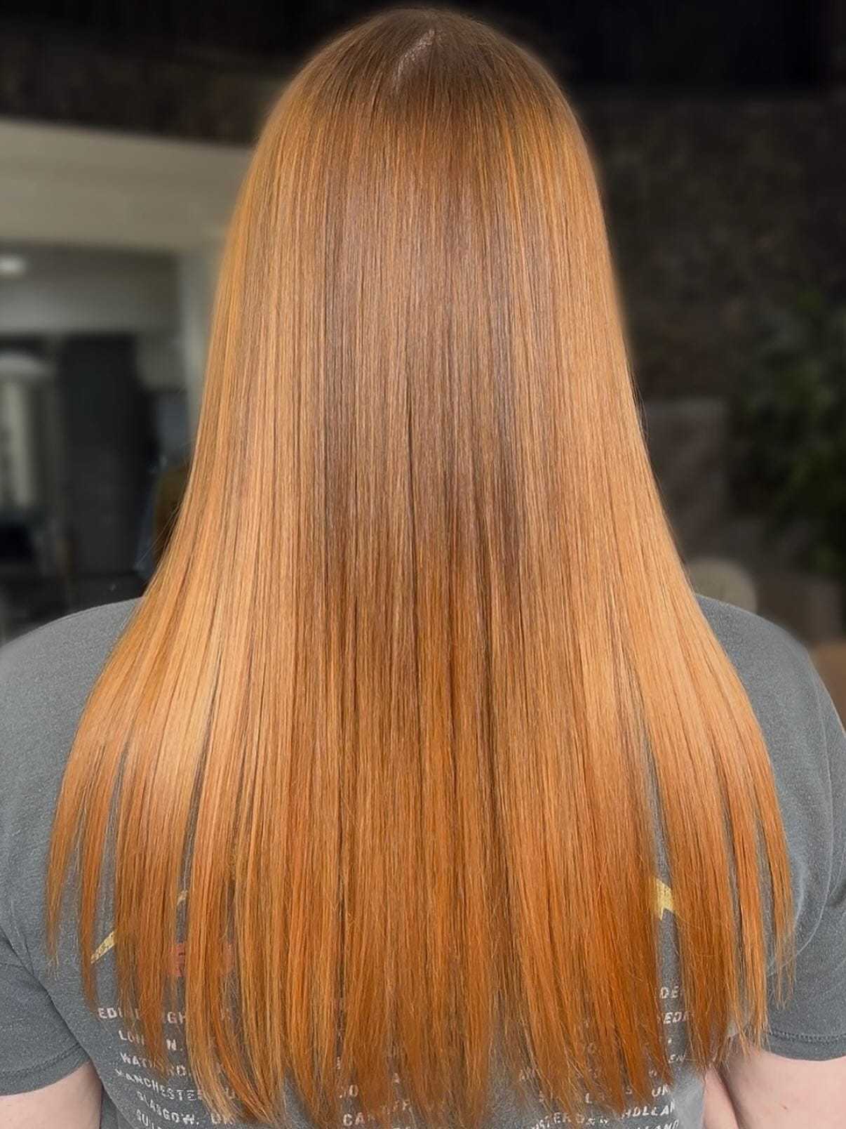 Long, straight auburn hair, viewed from the back, against a blurred indoor backdrop.