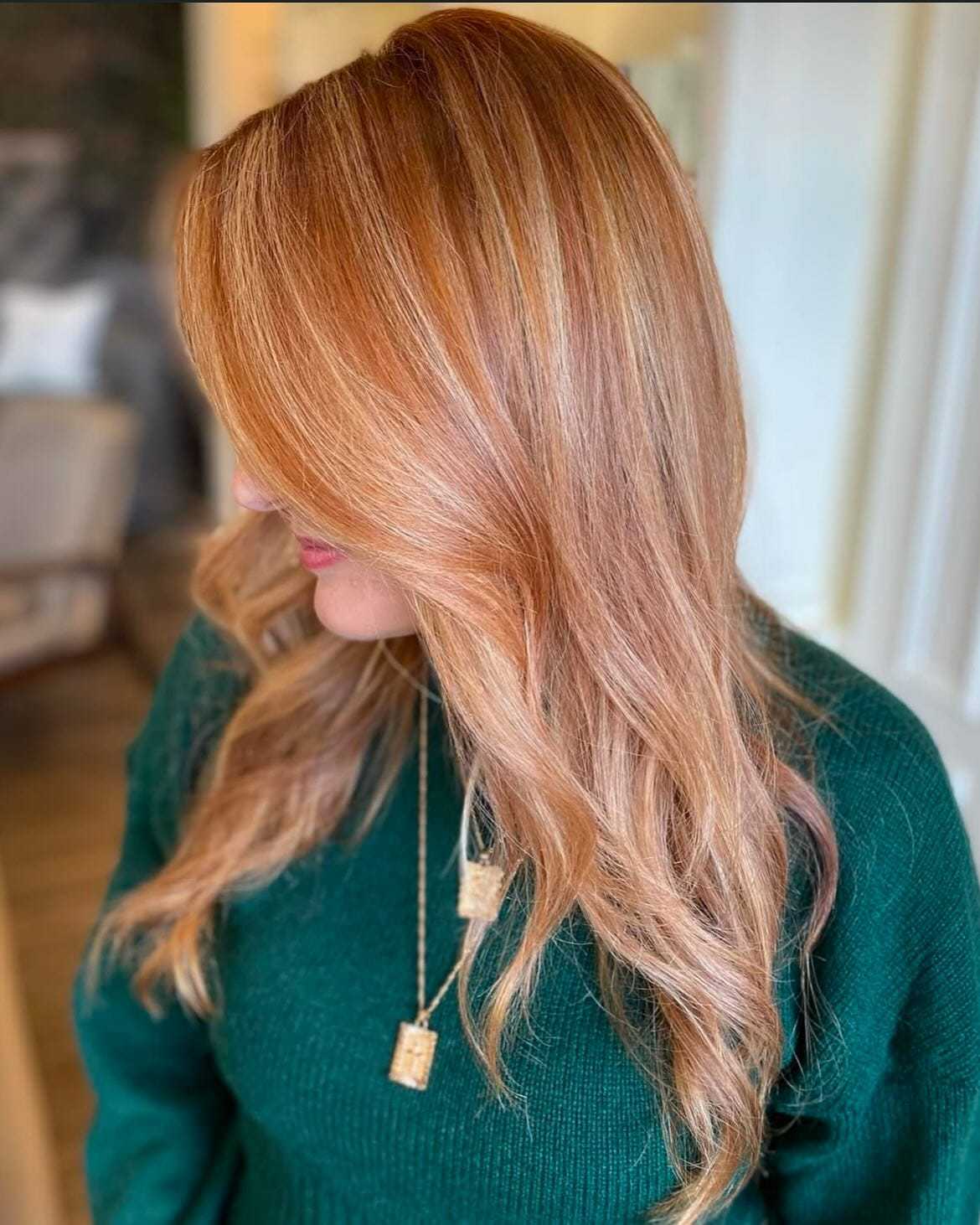 Woman with long, wavy, reddish-blonde hair in a green sweater, looking to the side.