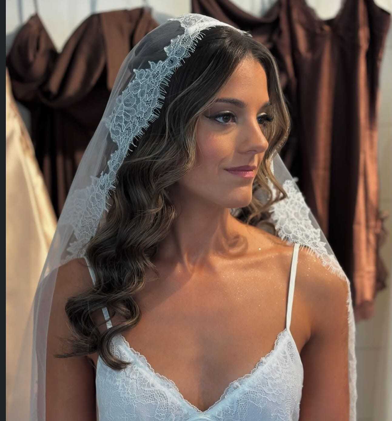 Bride wearing lace veil and white dress, surrounded by elegant brown gowns.